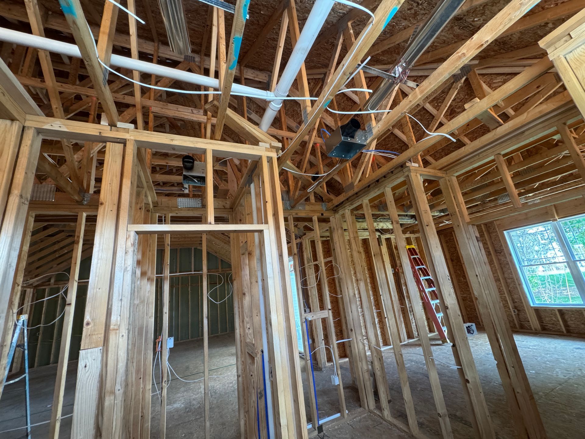 Interior view of a building under construction, showing wooden framing, exposed pipes, and wiring.
