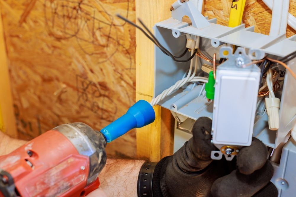 Electrician installing a light switch with a power drill and wire connections inside a wall.