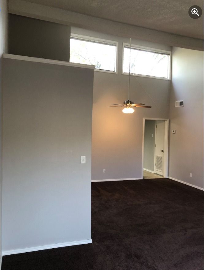 an empty living room with a ceiling fan and windows