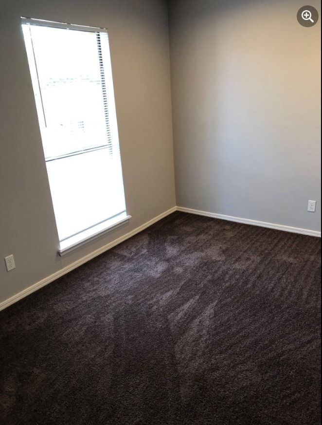 an empty bedroom with a window and brown carpet .