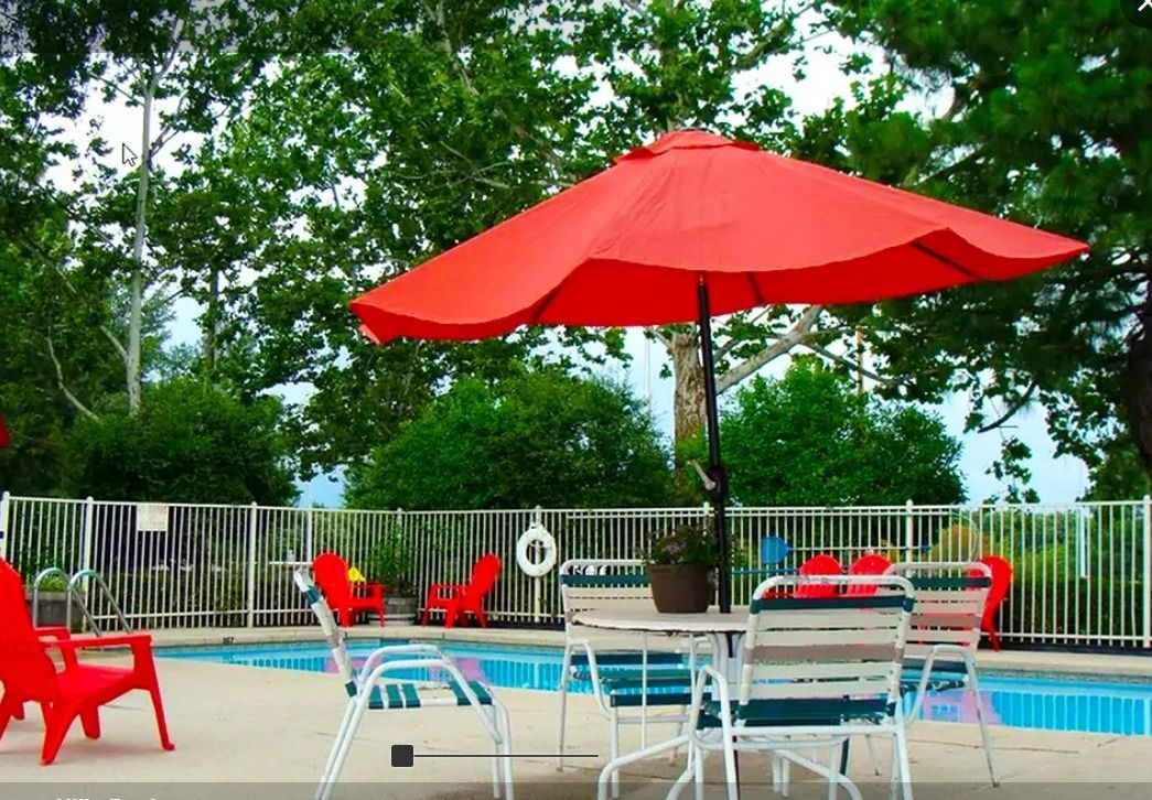a red umbrella sits in front of a swimming pool
