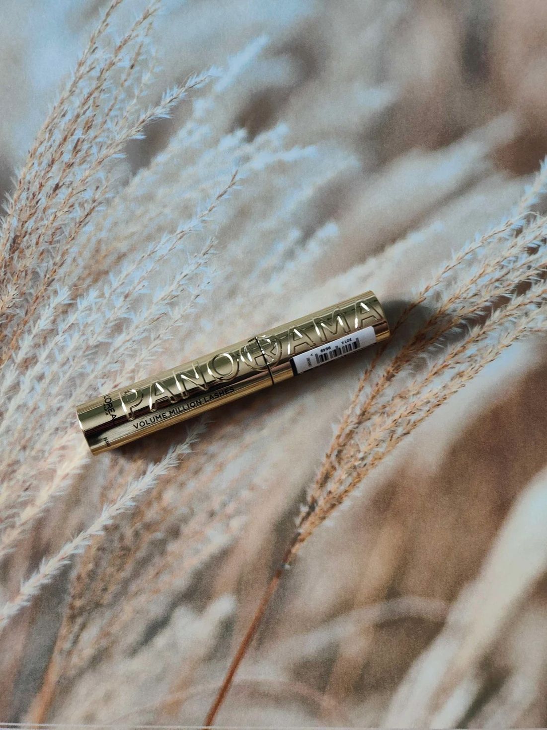 Golden mascara tube  on a background of beige feathery plants.