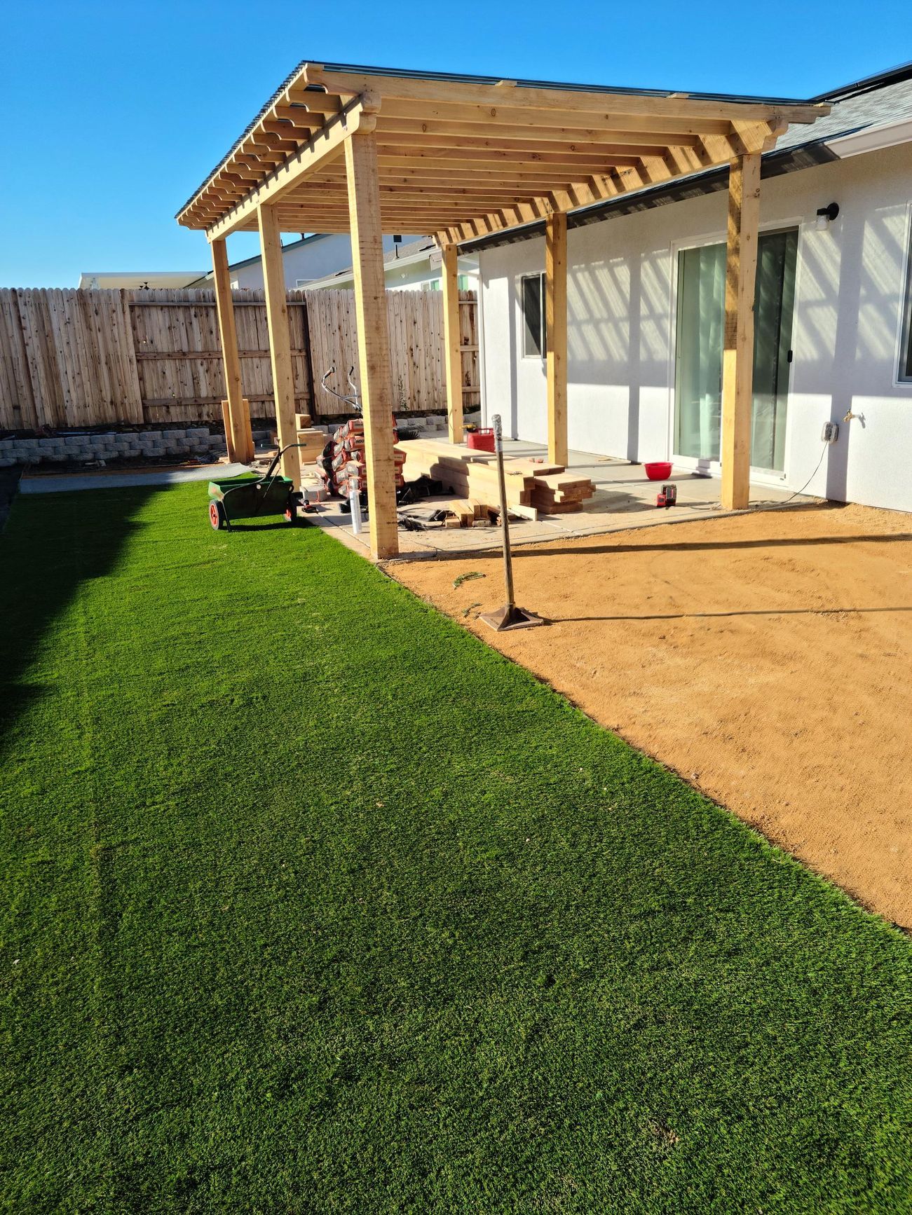 A wooden pergola under construction next to a house with a grass lawn and gravel area.