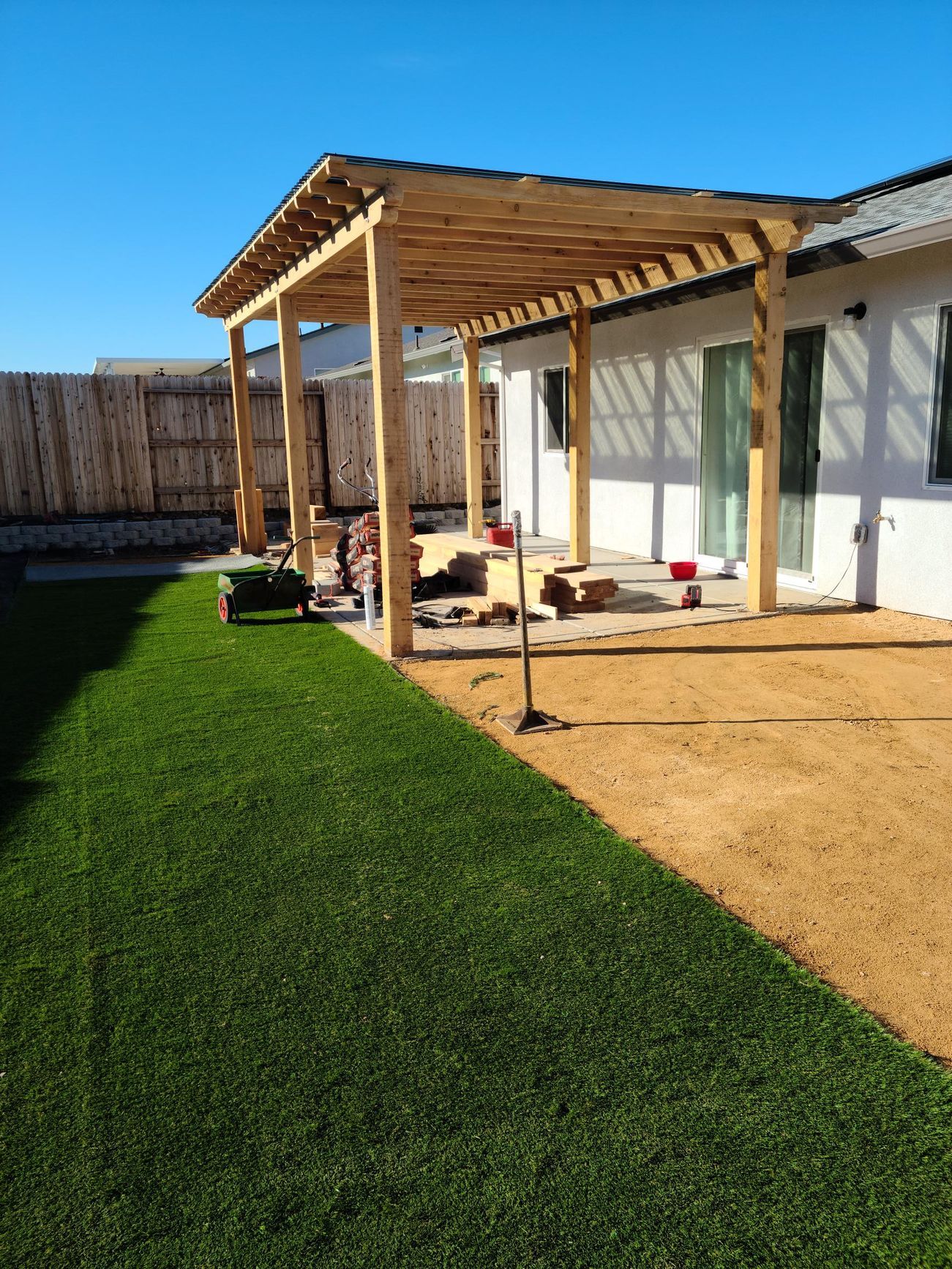 Pergola construction in a backyard with green grass and tan gravel.
