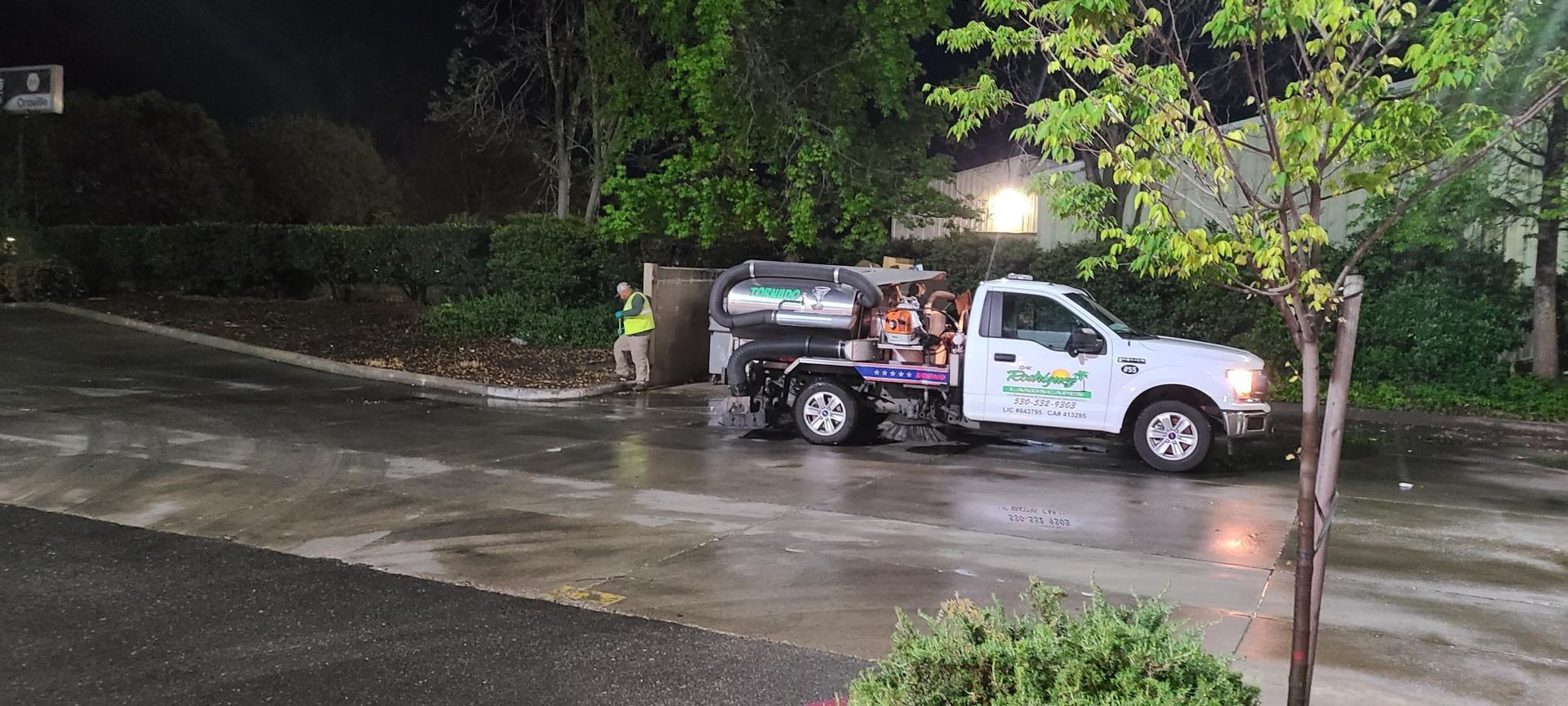 A truck with a work crew near a water access cover on a wet road at night.