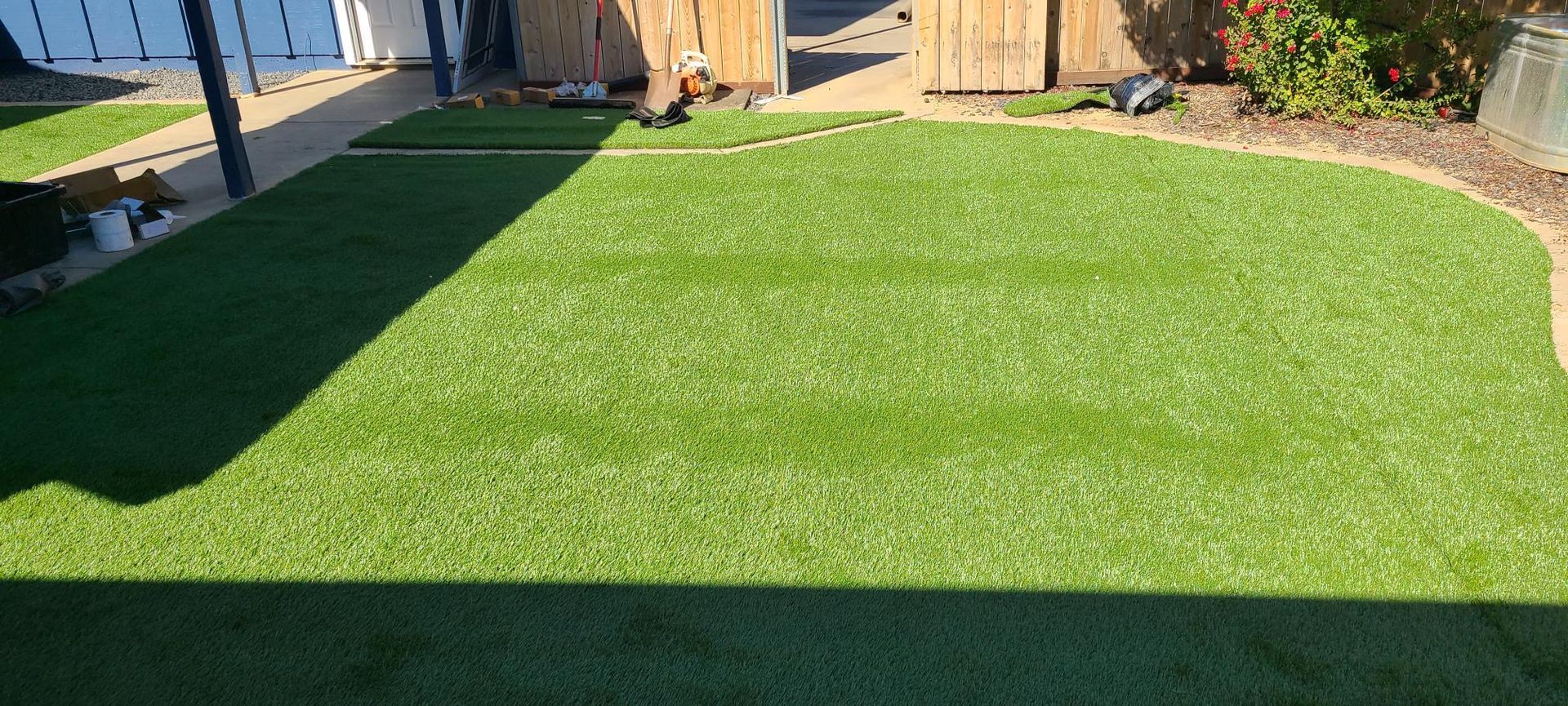 Green turf with a paved walkway, fence, and a glimpse of a body of water in the background.