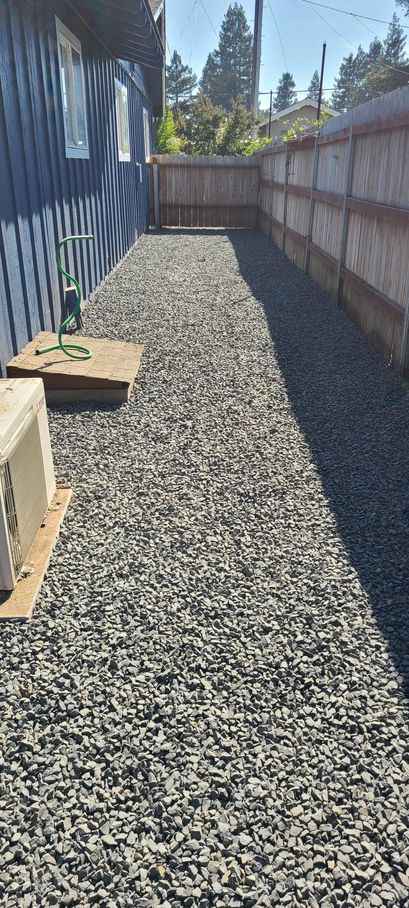 A narrow gravel path runs between a blue house and a wooden fence.