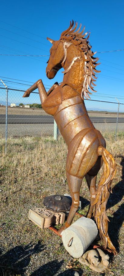 A rusty metal horse sculpture rearing up outdoors, against a blue sky and grass.