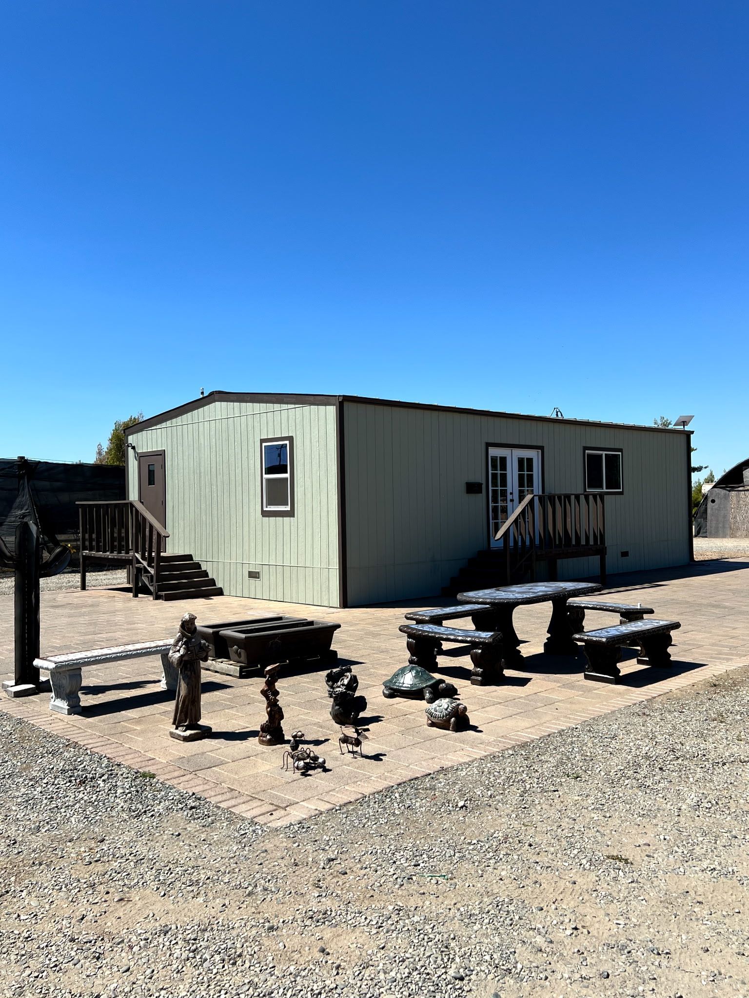 A single-story, pale green building with picnic tables, benches, and figurines under a clear blue sky.