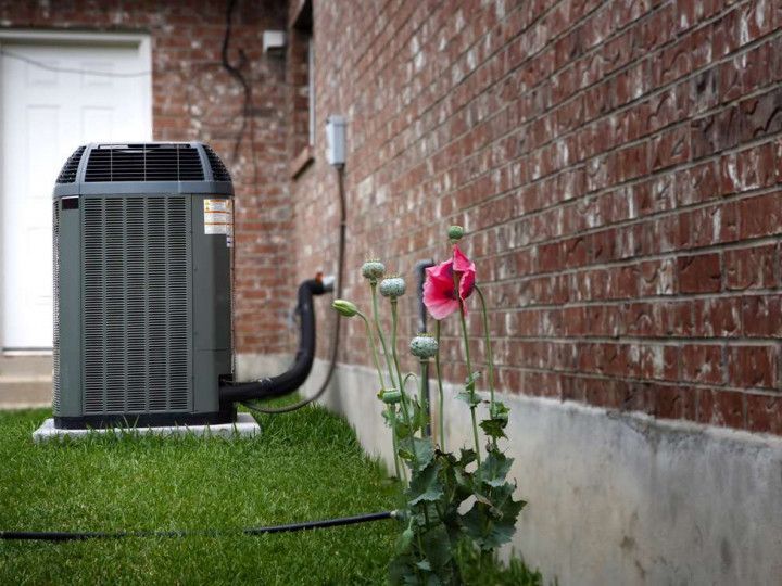 An air conditioner is sitting on the side of a brick building next to a flower. HVAC company in Gresham OR