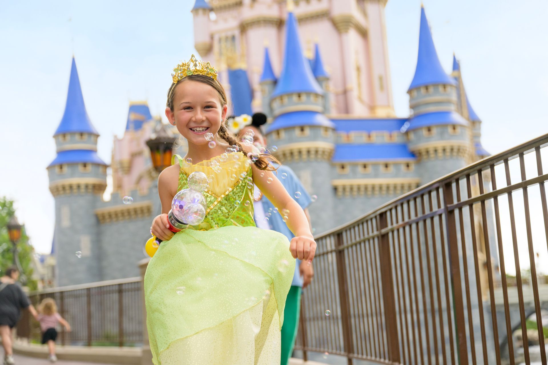 Girl in princess dress blows bubbles near Cinderella's castle at Disney World.
