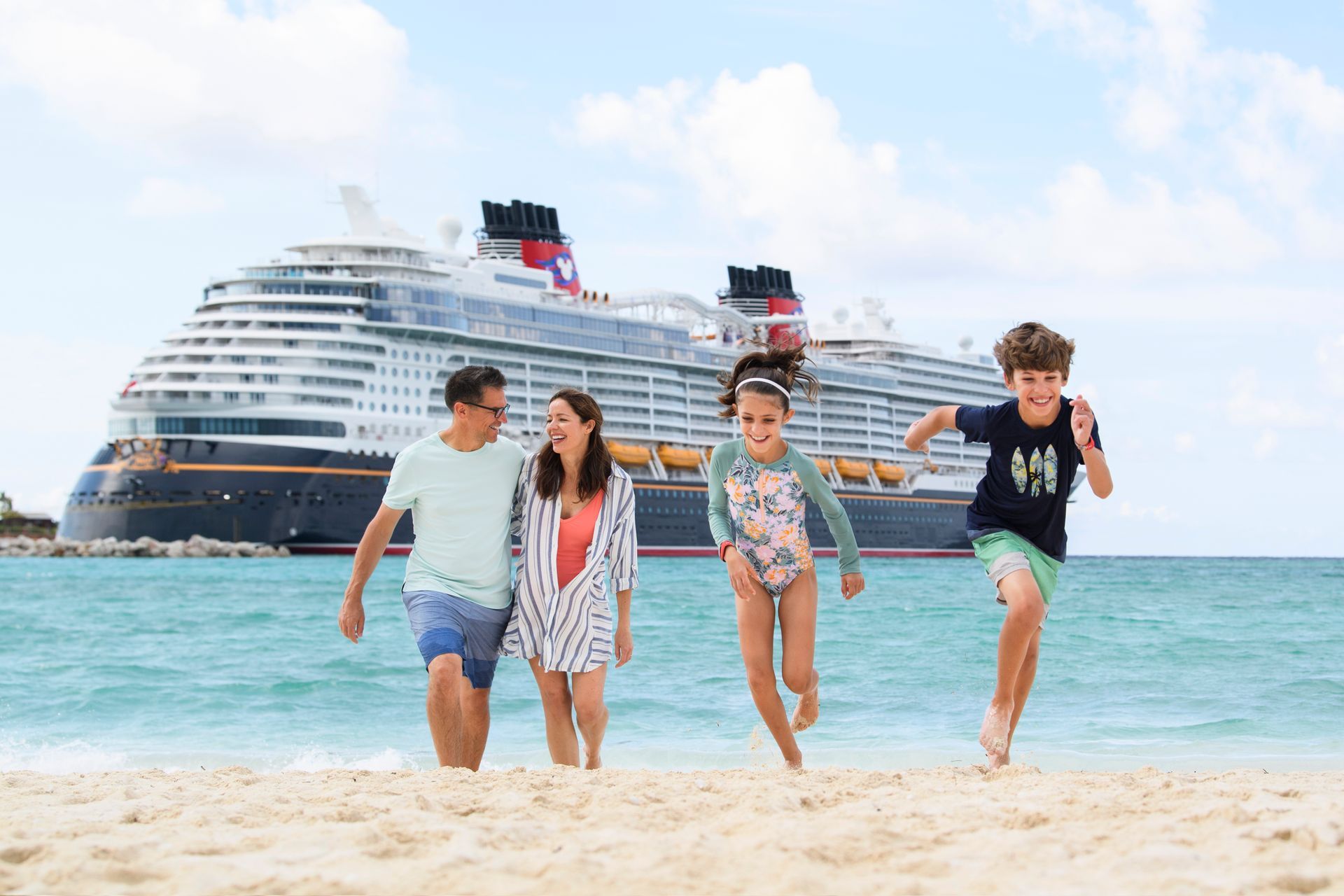 Family running on beach in front of a Disney cruise ship; blue sky, sunny day.