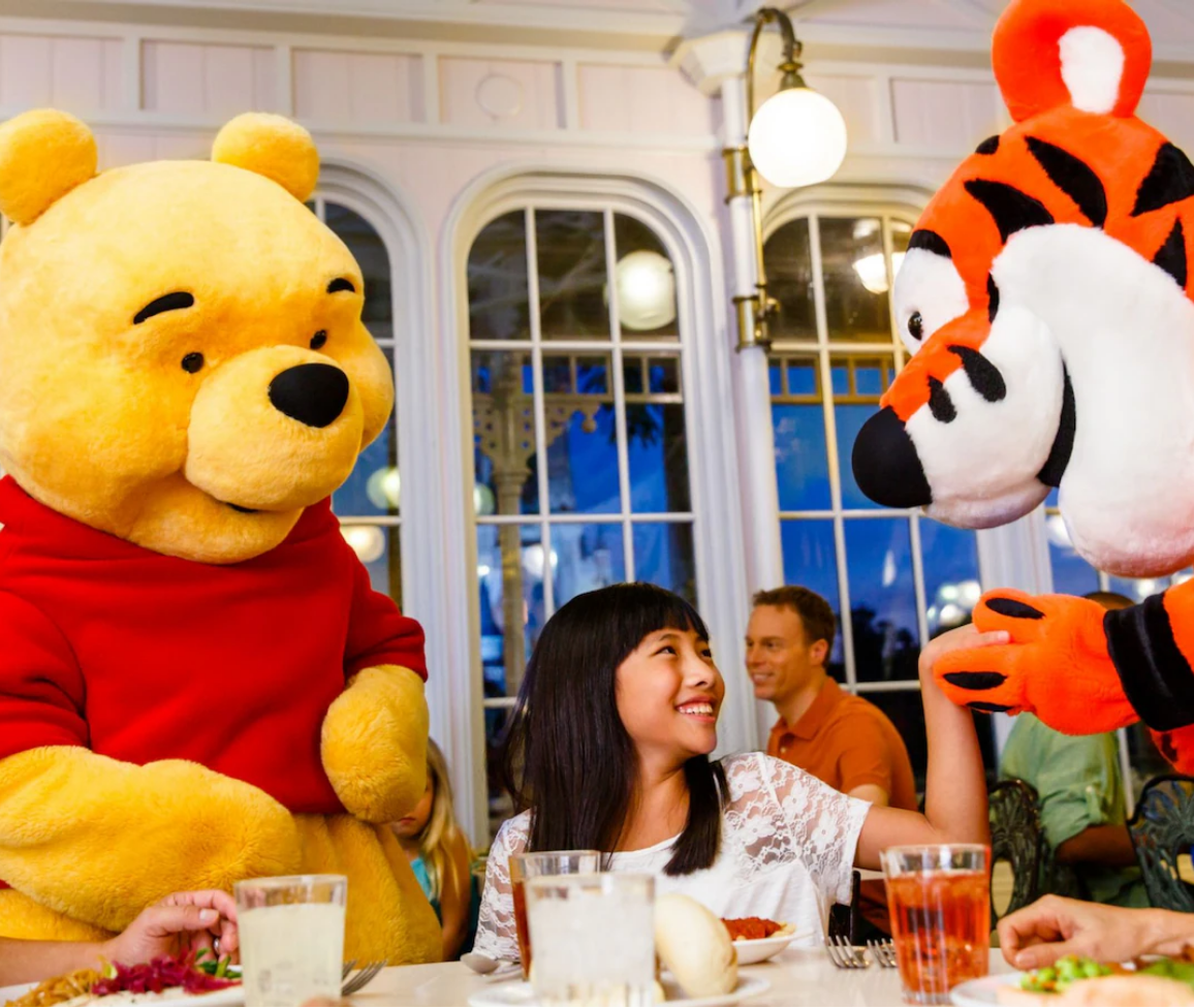 A girl sits at a table with a winnie the pooh and tigger mascot