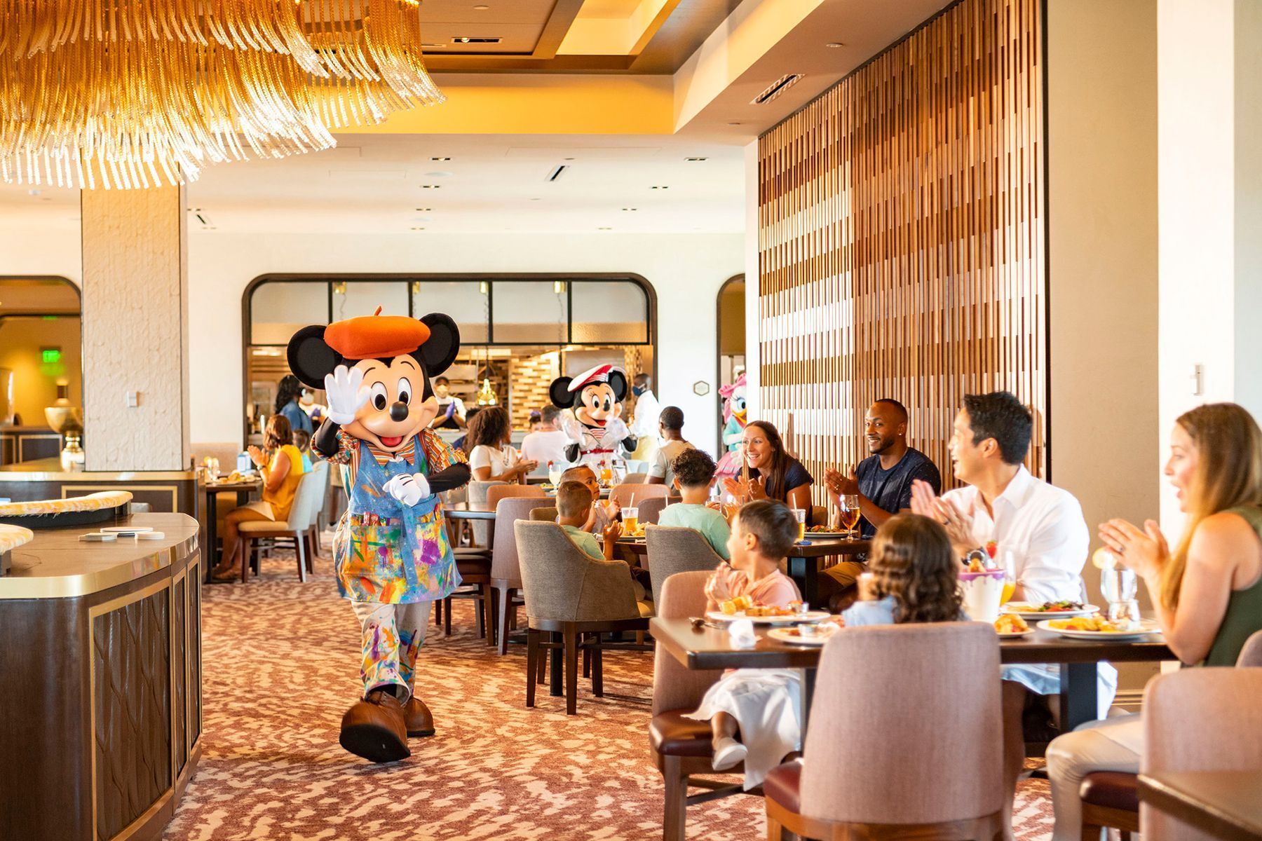Mickey mouse and minnie mouse are standing in a restaurant with people sitting at tables.
