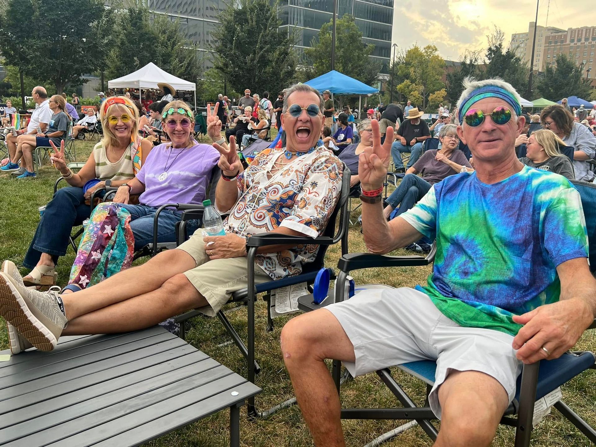 A group of people are sitting in chairs dressed in tie-dye and hippie outfits