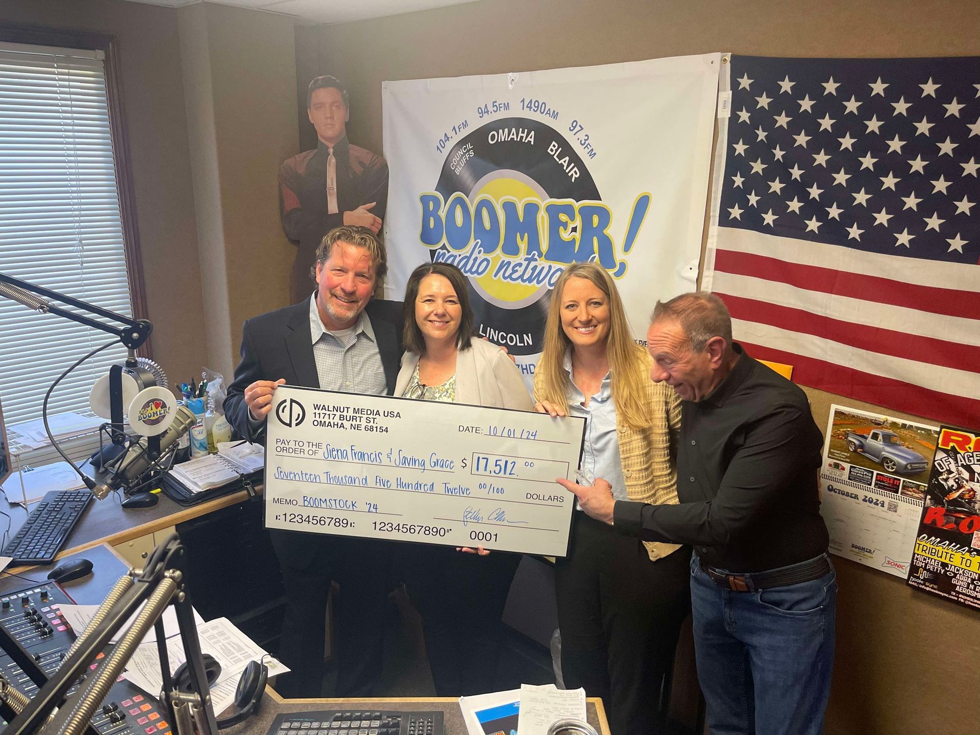 A group of people are holding a large check for Sienna Francis House and Saving Grace in a radio studio.