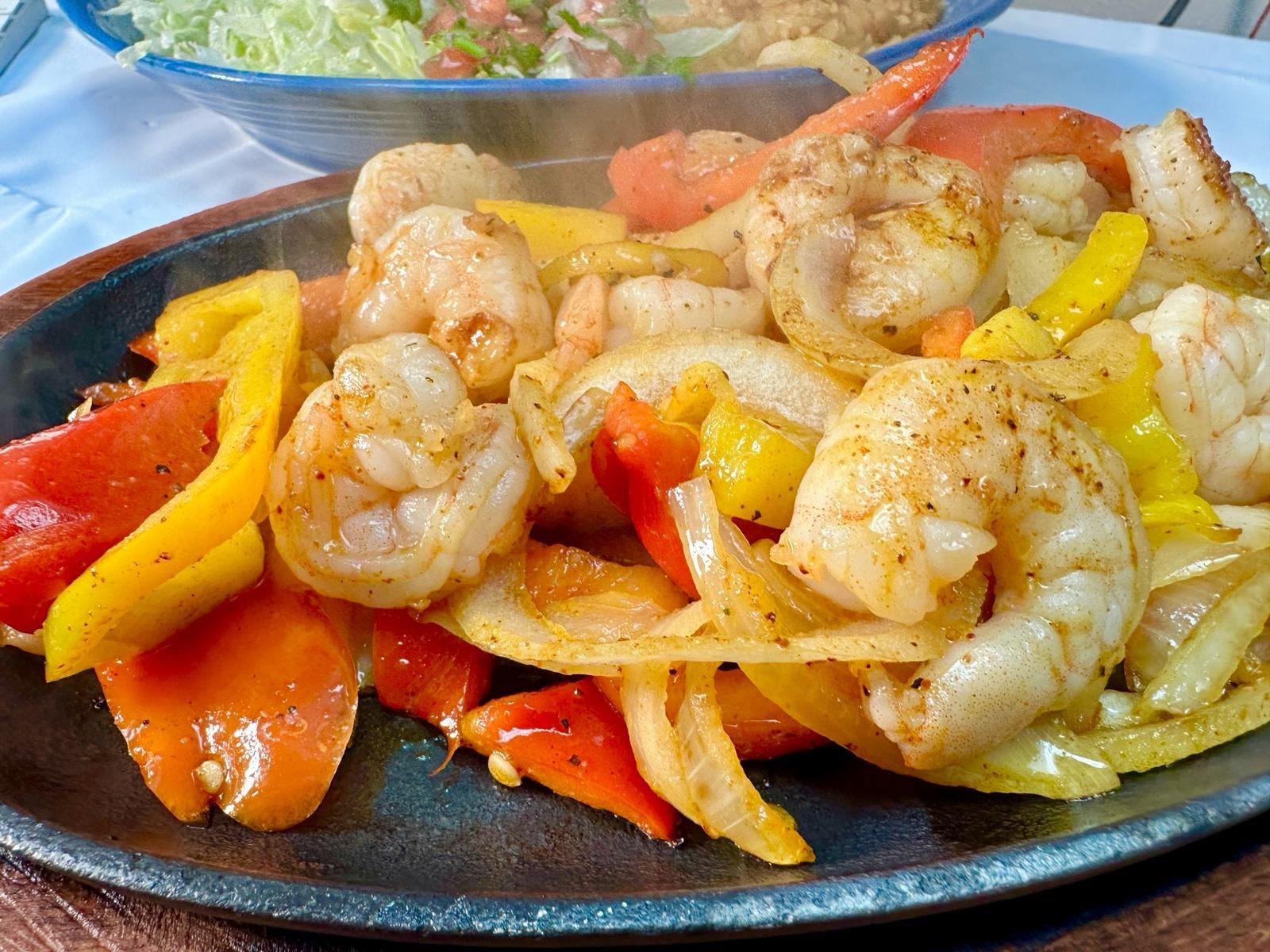 Sizzling shrimp fajitas with colorful peppers and onions on a dark plate, steam rising.
