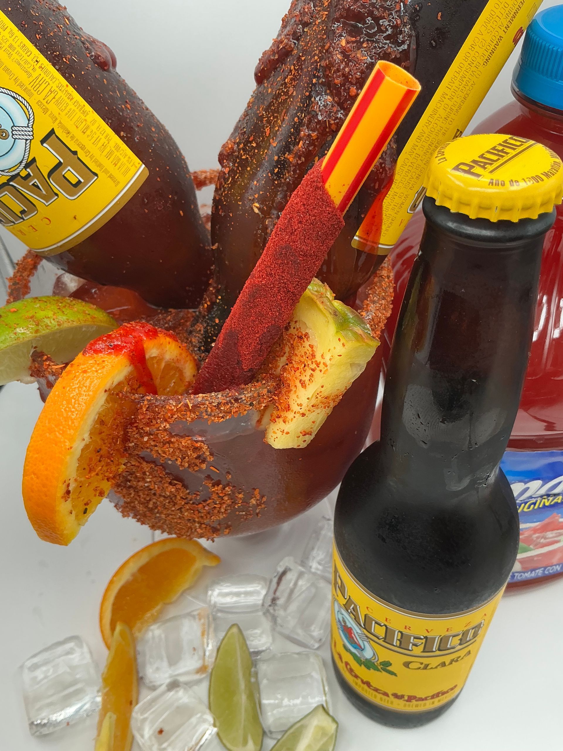A refreshing michelada with Pacifico beer bottles, lime, orange slices, and spicy candy stick.