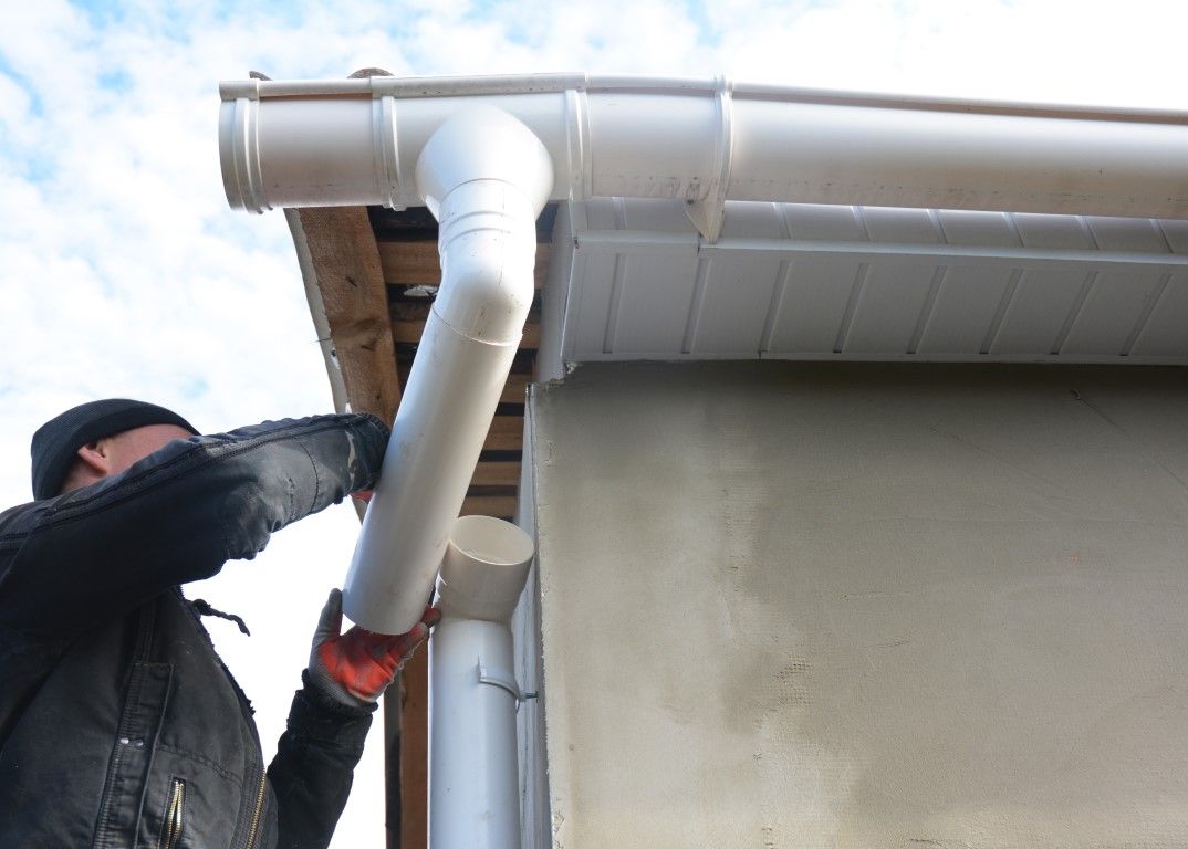 Person installing a white gutter downspout on a building.