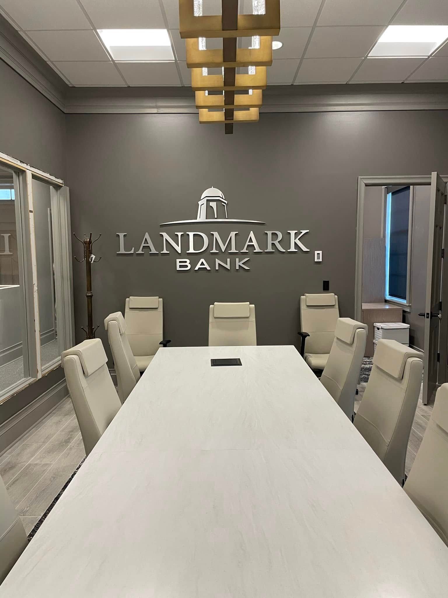 Meeting room with white table, chairs, gray walls, and Landmark Bank logo.