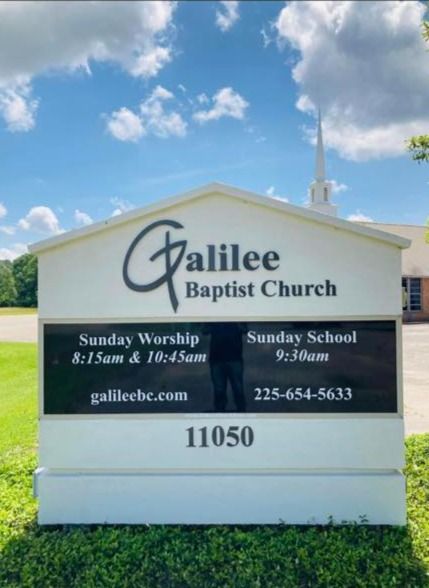 Sign for Galilee Baptist Church with service times, website, and phone number; white with black lettering, outdoors.