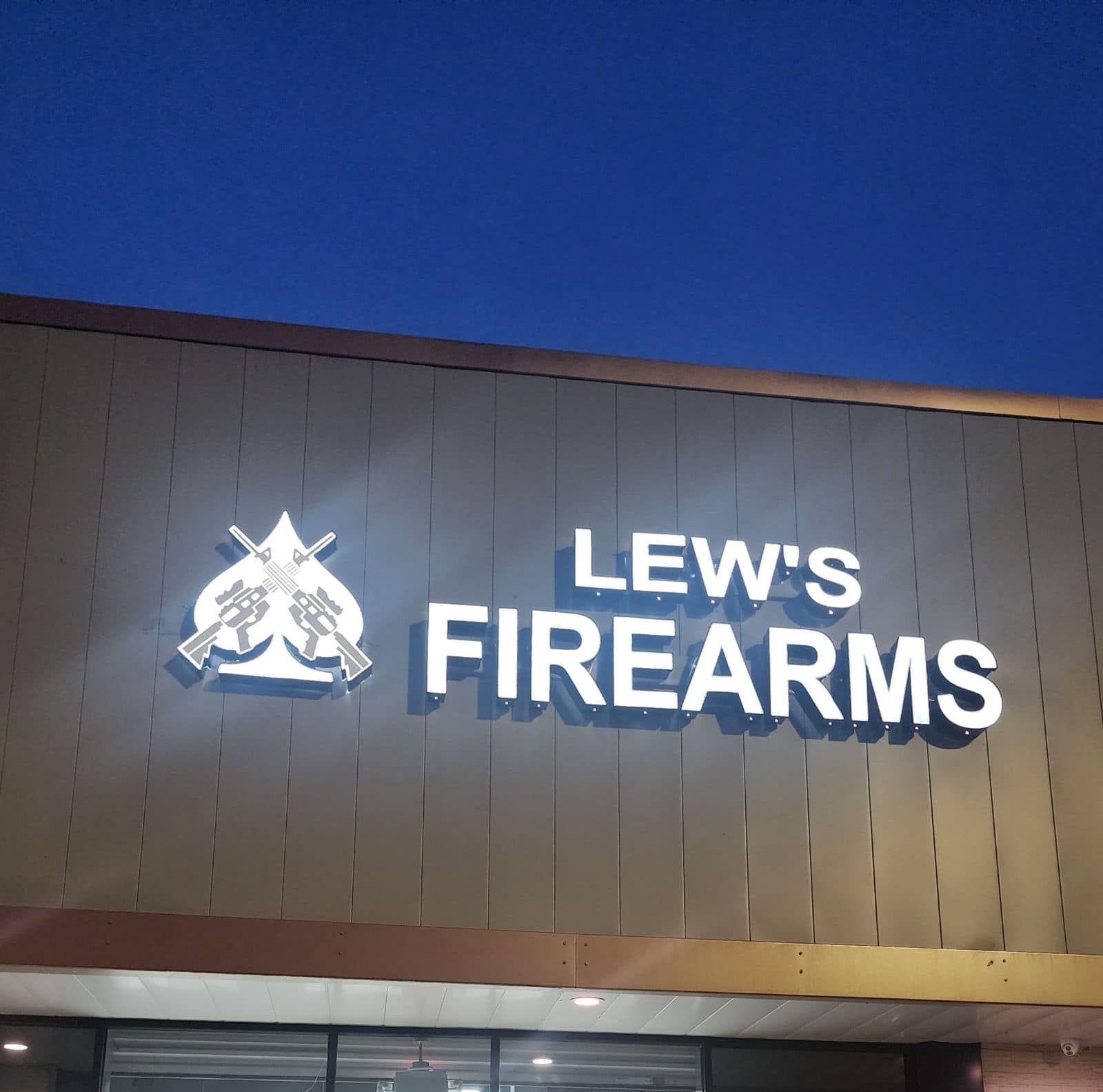Lew's Firearms store sign with logo of crossed rifles, white text on beige building exterior.