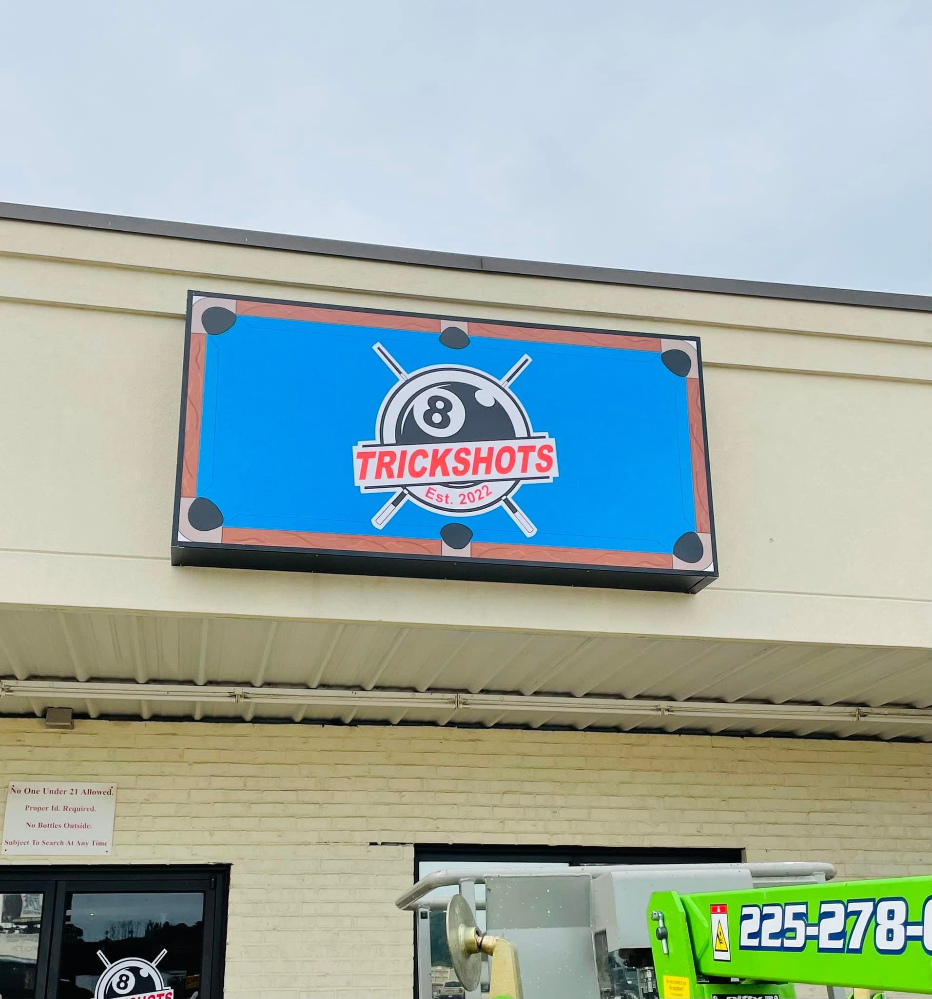 Sign for Trickshots pool hall with a blue pool table background and logo.