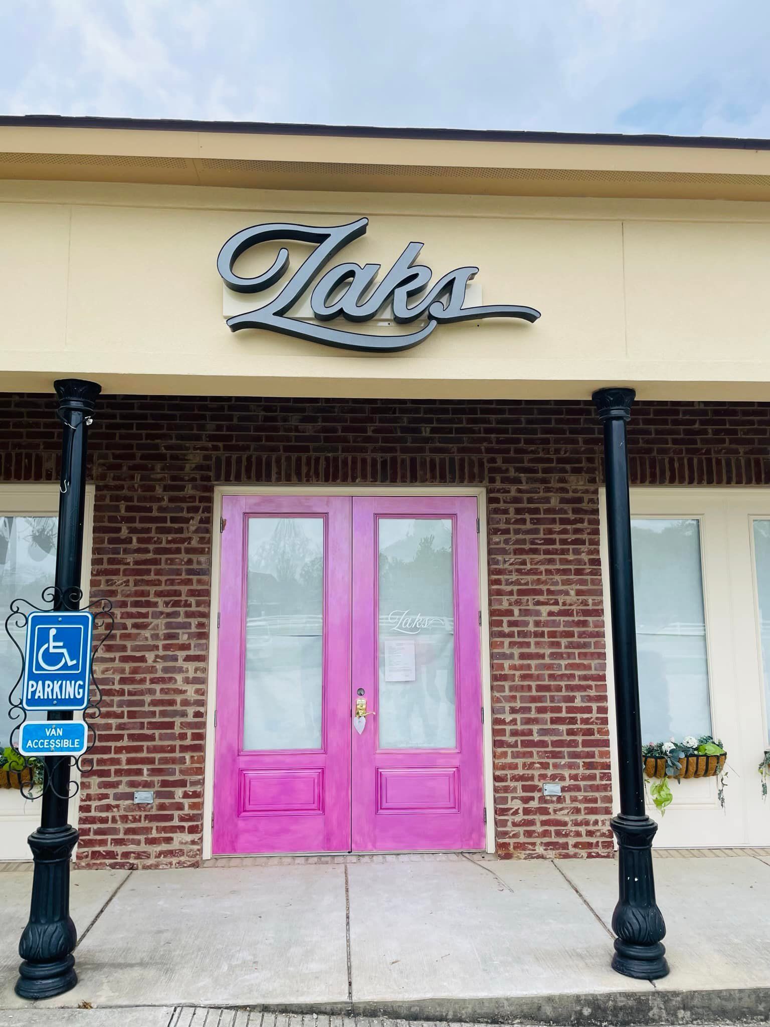Taks restaurant entrance with bright pink double doors, brick facade, and accessible parking sign.