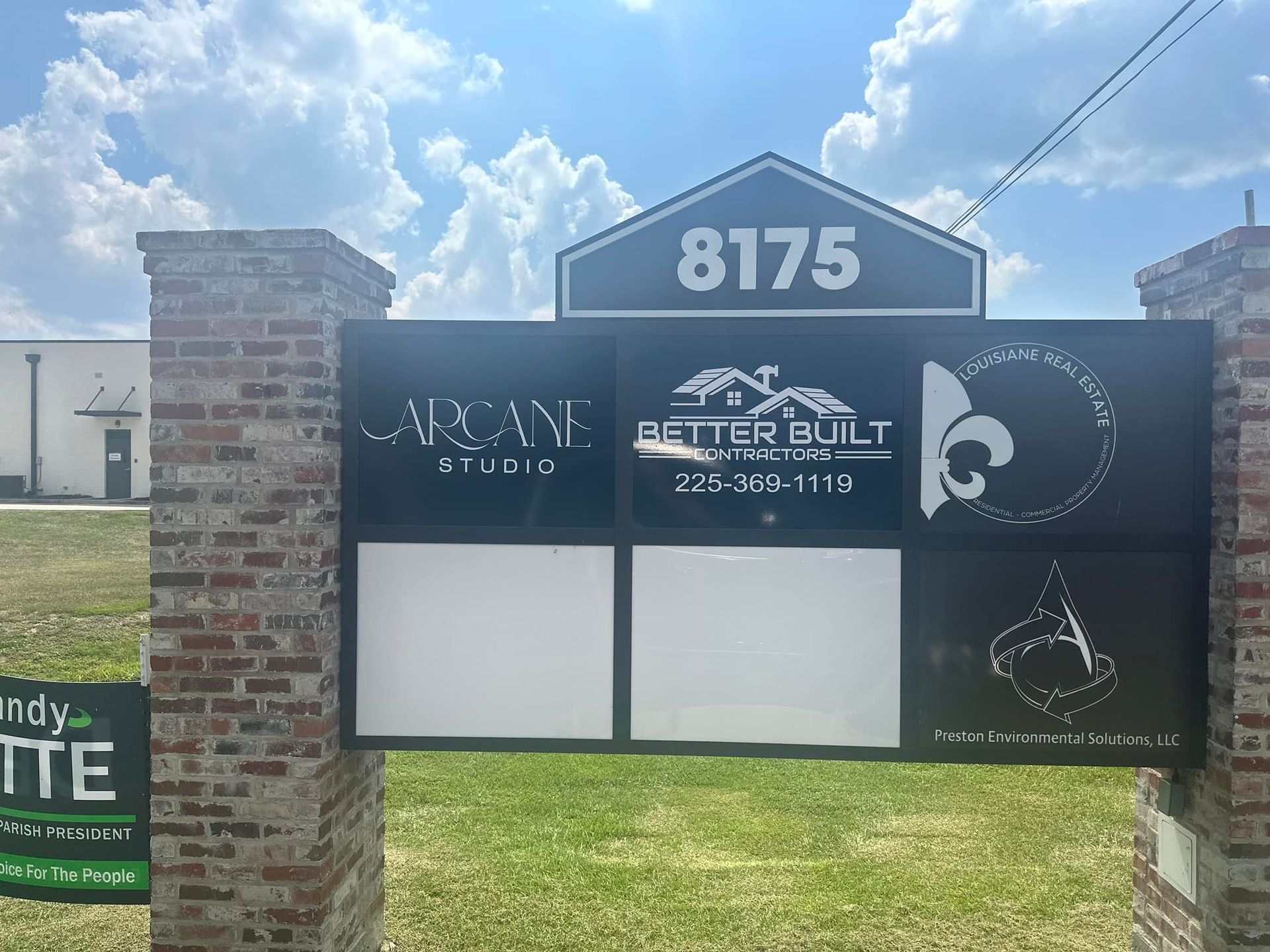 Sign with business logos, street address 8175, on brick pillars; bright, sunny day.