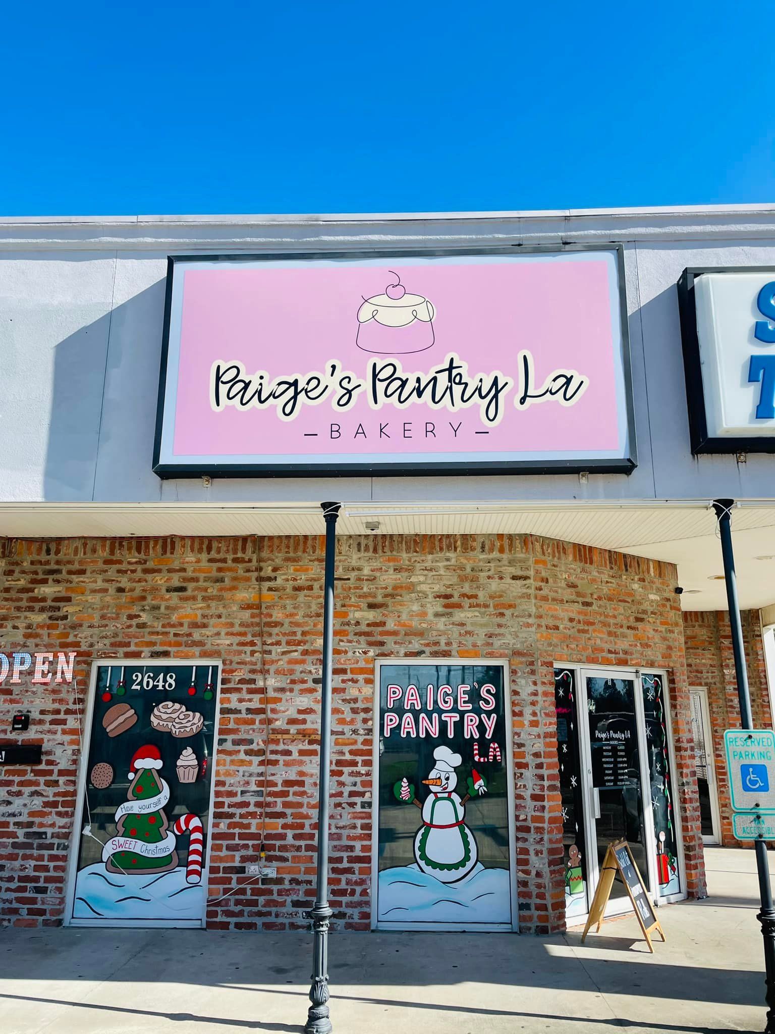 Exterior of Paige's Pantry, a bakery, with a pink sign. Two doors have winter-themed artwork.