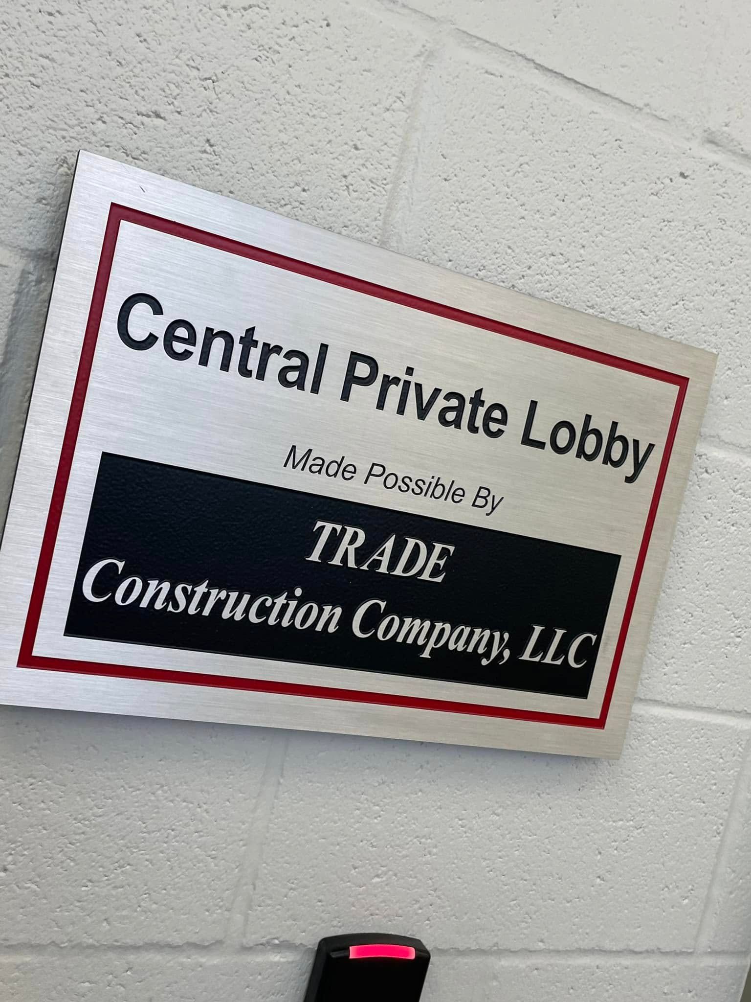 Sign for Central Private Lobby, sponsored by Trade Construction Company, LLC. Silver, black, and red signage.