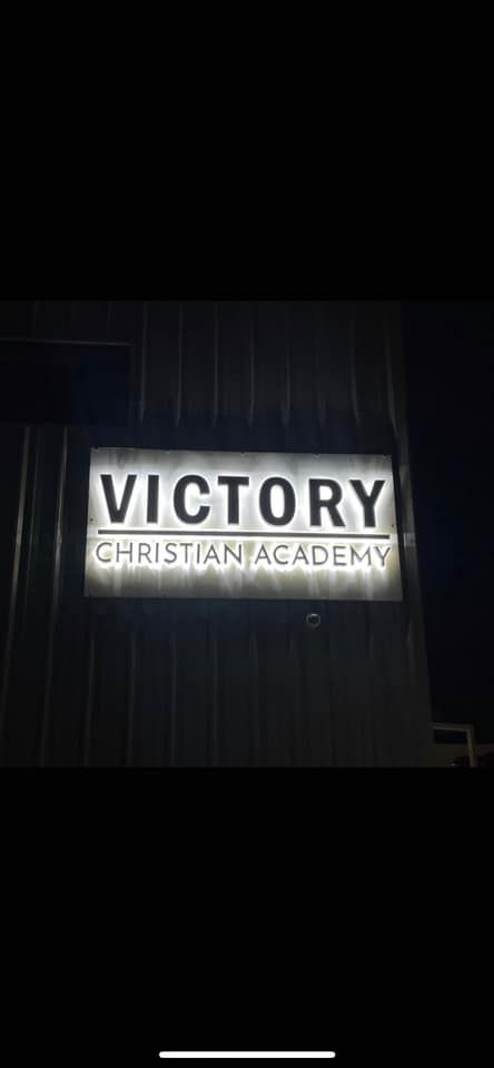 Illuminated sign for Victory Christian Academy at night.