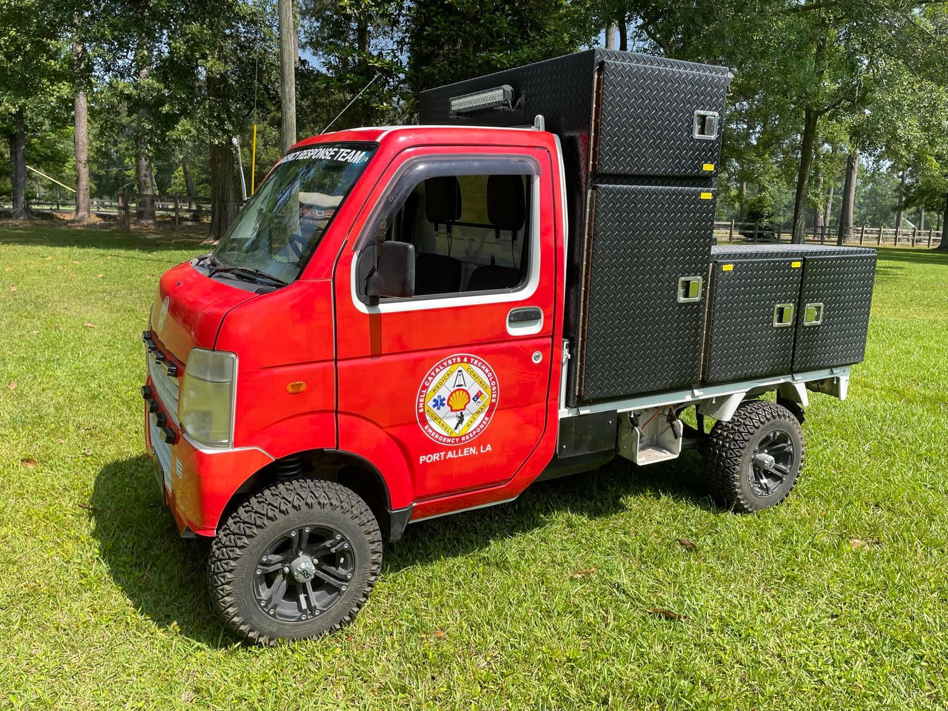 Red mini truck with black sound equipment in a grassy field.