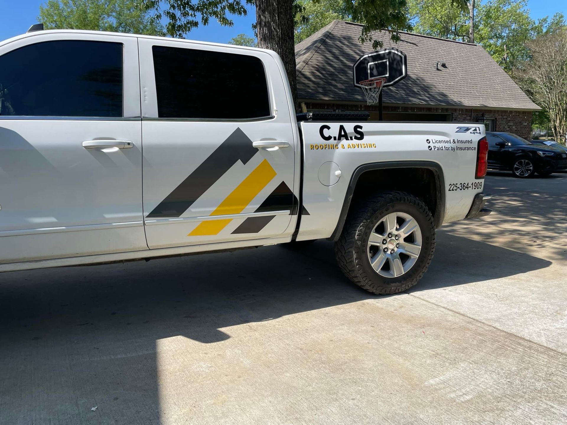 White pickup truck with C.A.S. logo, parked on a concrete driveway in front of a house.