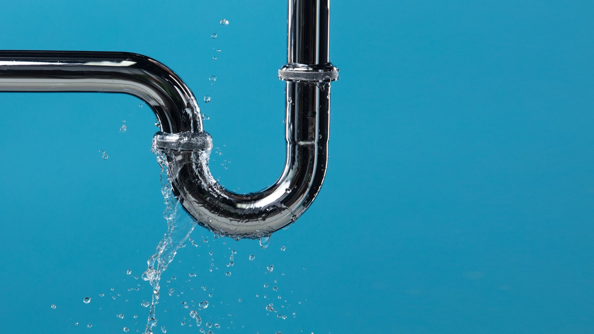 Water leaking from a joint in a chrome pipe against a solid blue background.