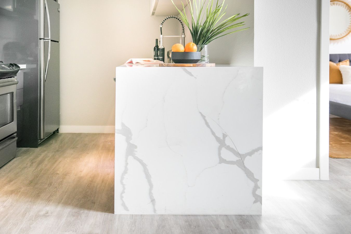 A white kitchen island with gray marble-like veining stands in a bright, modern room with light wood flooring.