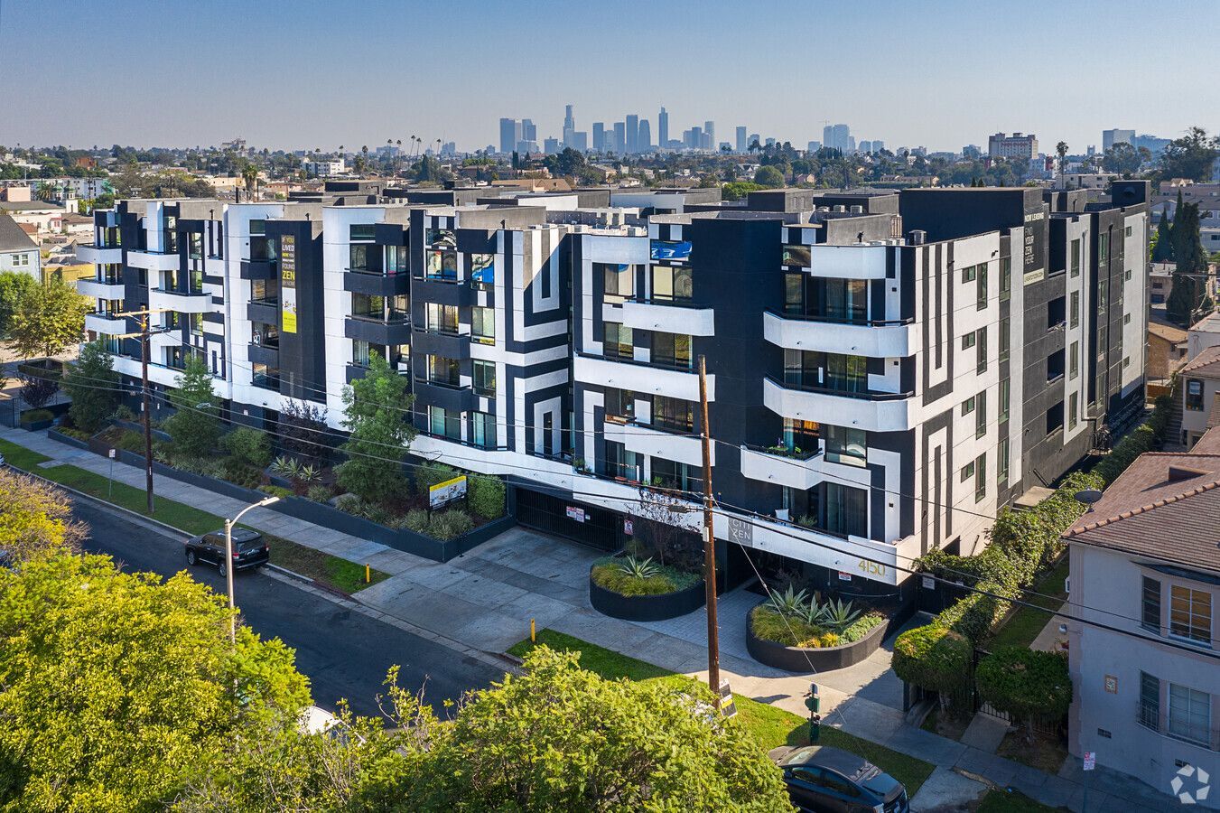 A modern, black-and-white apartment complex with balconies, viewed from above, featuring the Los Angeles skyline behind.