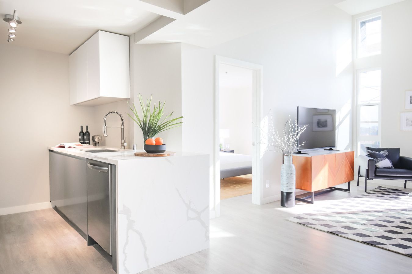 A bright, modern studio apartment featuring a stainless steel kitchen island, an open living area, and a bedroom doorway.