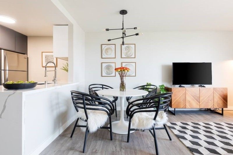 A modern dining area with a white pedestal table, four black bentwood chairs with faux-fur throws, and a light wood sideboard.