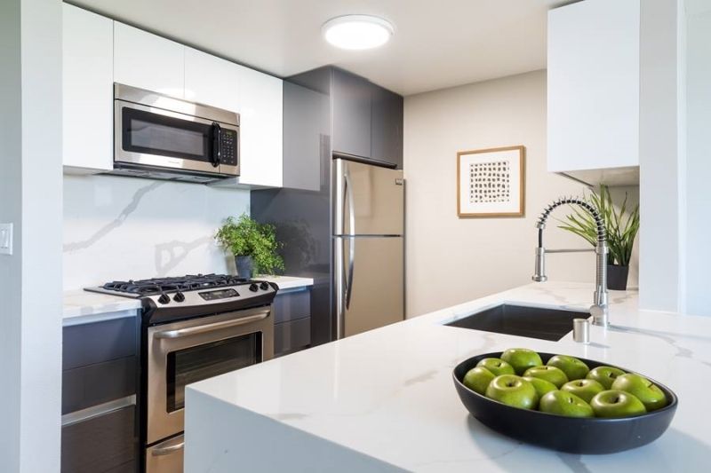 Modern kitchen with white and dark gray cabinets, stainless steel appliances, and a bowl of green apples on an island.