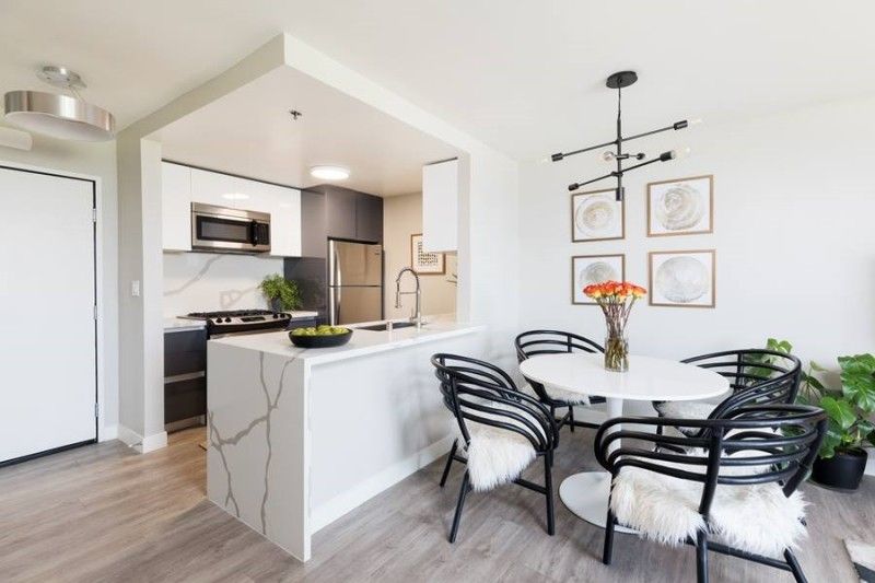 A bright, modern kitchen and dining area with white marble countertops, black wicker chairs, and a white round table.