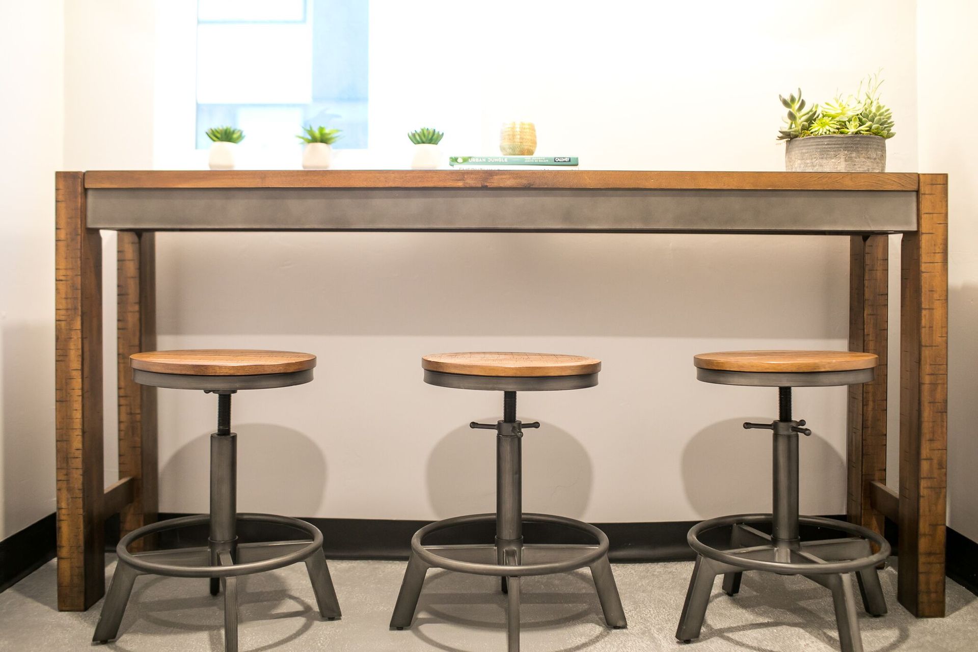 A tall, rustic wooden bar table with three matching swivel stools featuring wood seats and gray metal bases.
