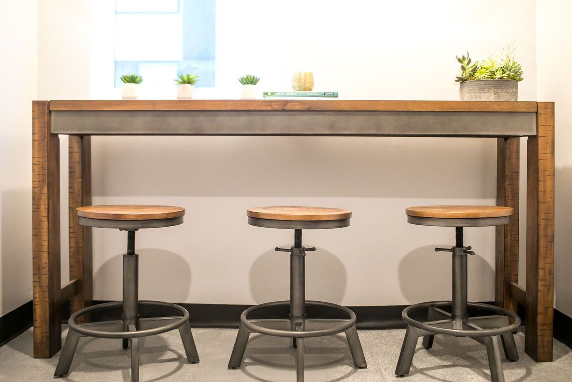 A tall, rustic wooden bar table with three matching swivel stools featuring wood seats and metal bases against a wall.