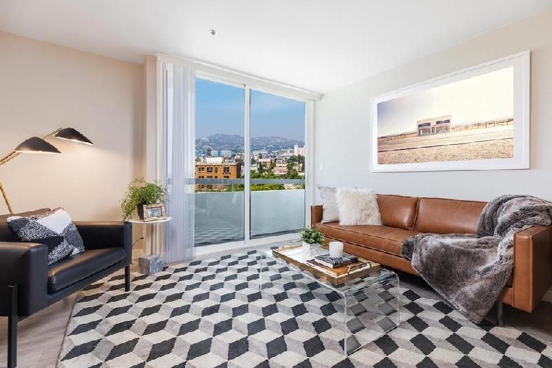 A modern living room with a brown leather sofa, black armchair, geometric area rug, and a large framed desert landscape.