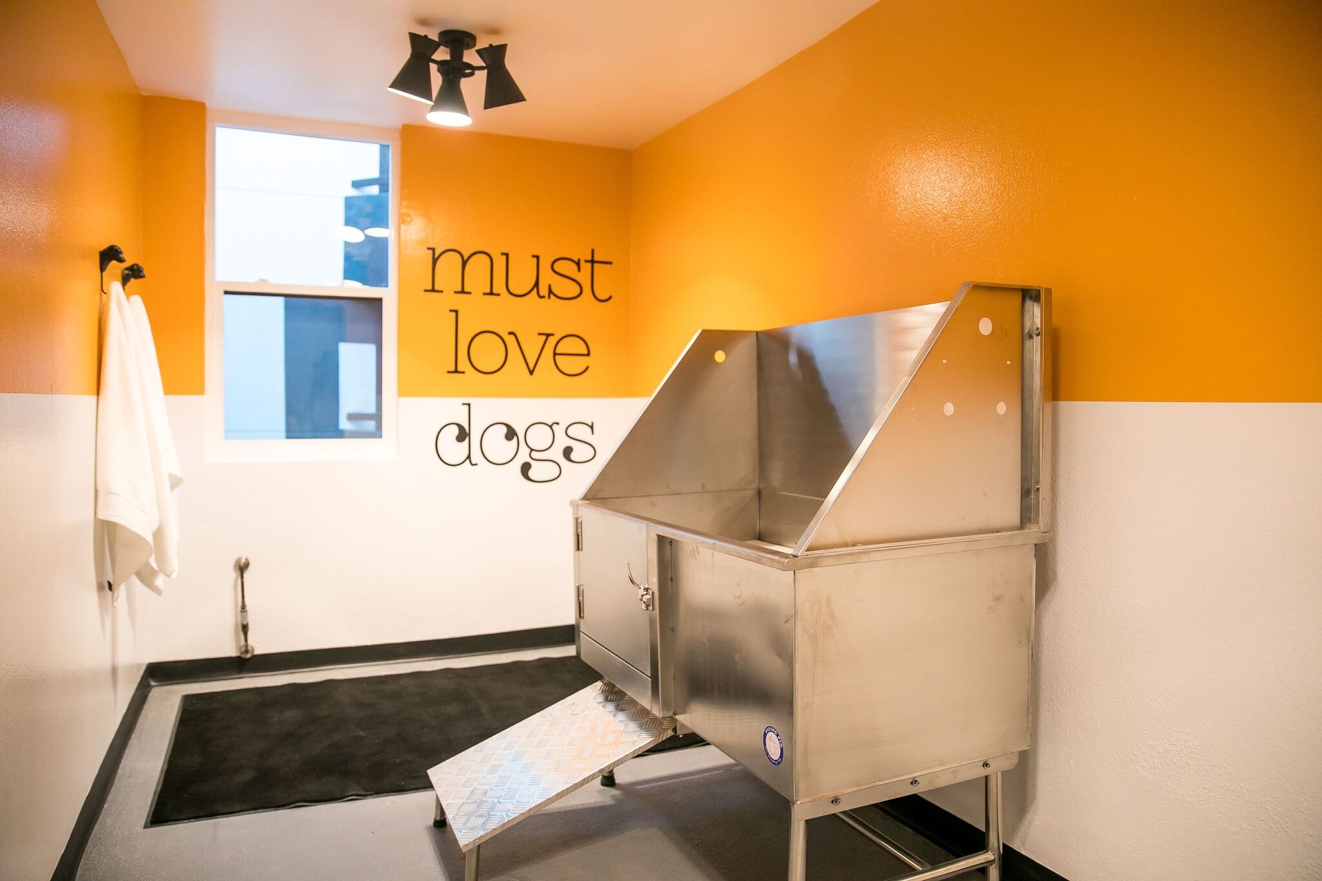 A pet grooming station with a metal tub and ramp, painted yellow and white, with the text 