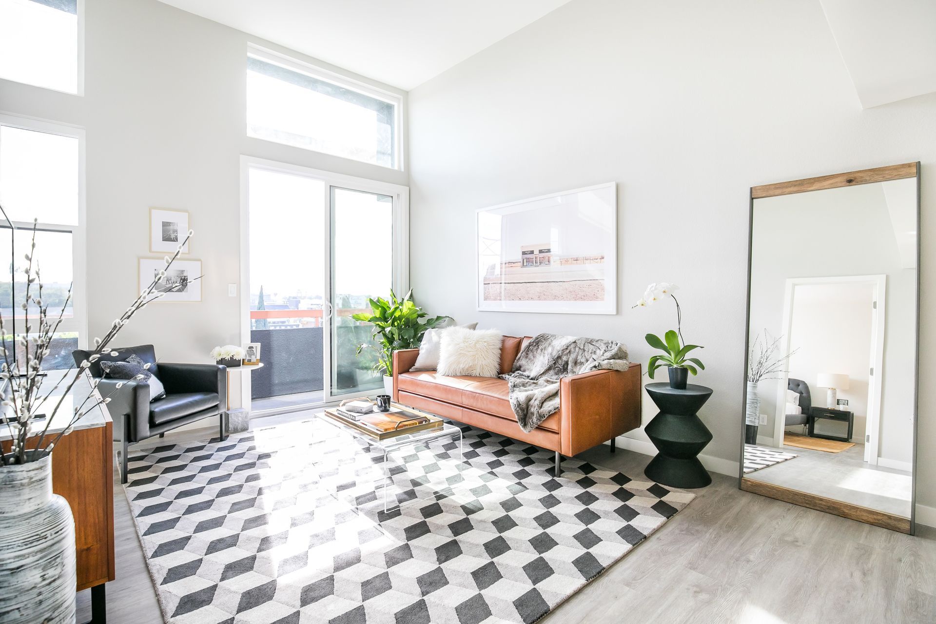 A modern living room with a brown leather sofa, black-and-white geometric rug, and a large floor mirror.