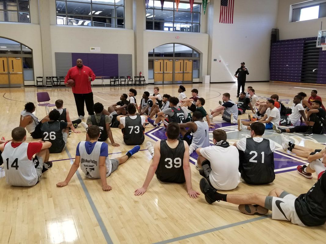 A group of basketball players are sitting on the floor in a gym.