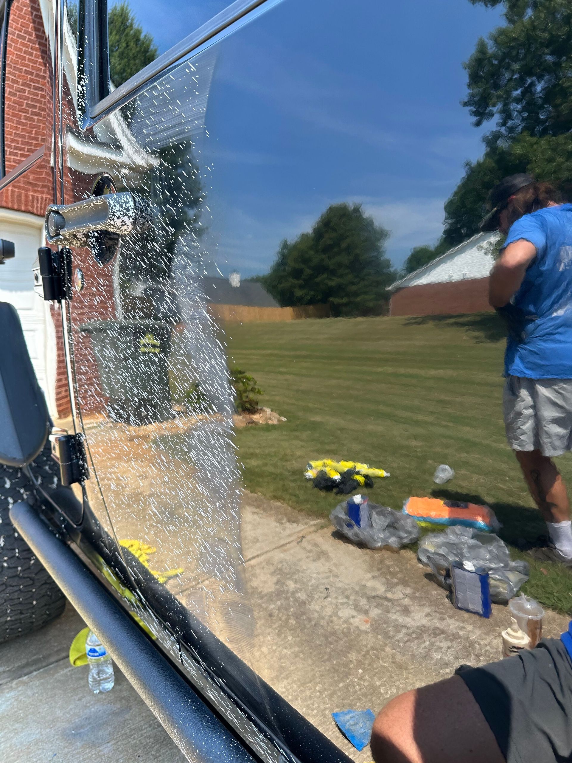Person applying tint to a vehicle window, working outside on a sunny day.