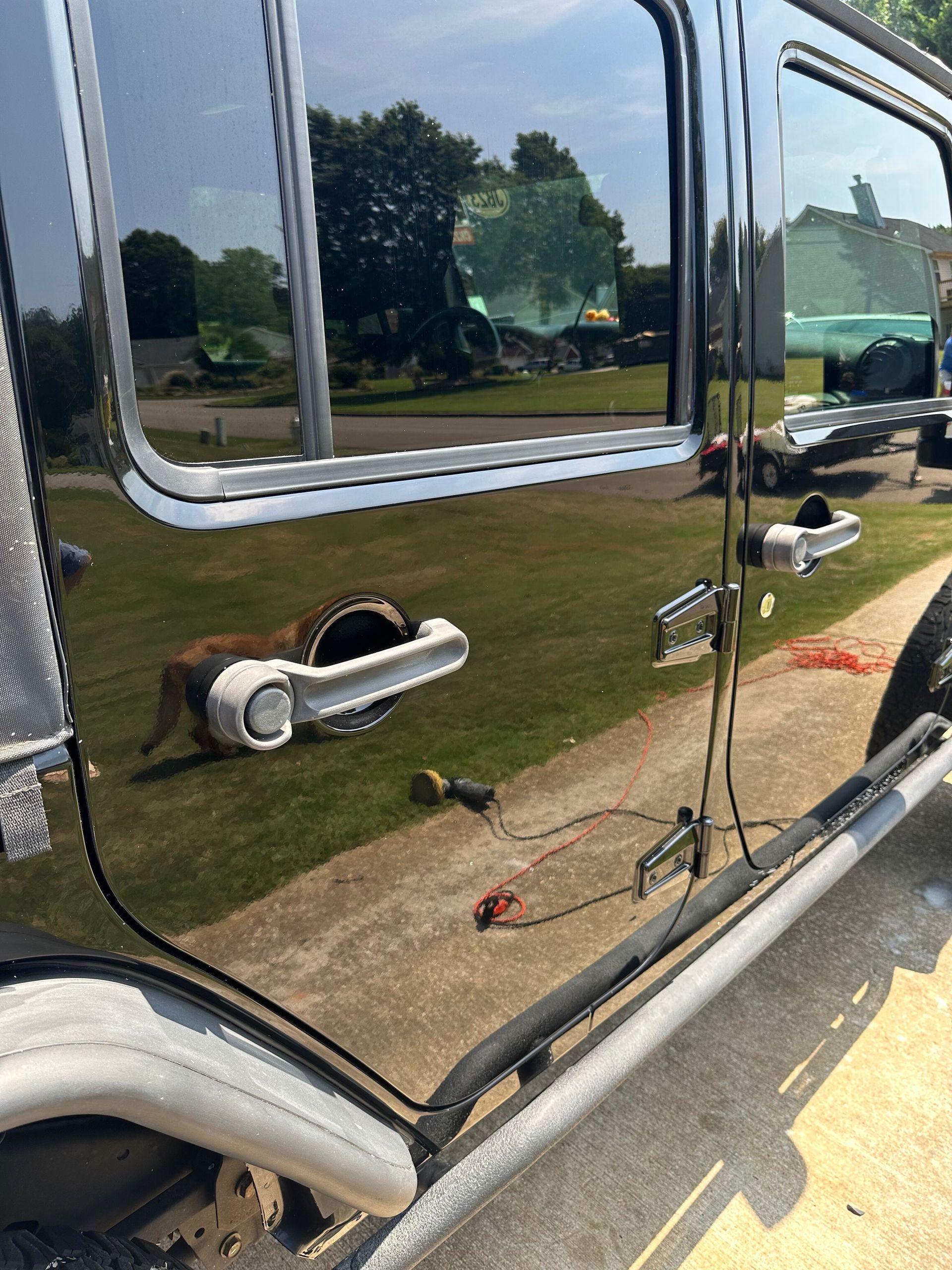 Black Jeep side with reflection of a dog, a house and green lawn.