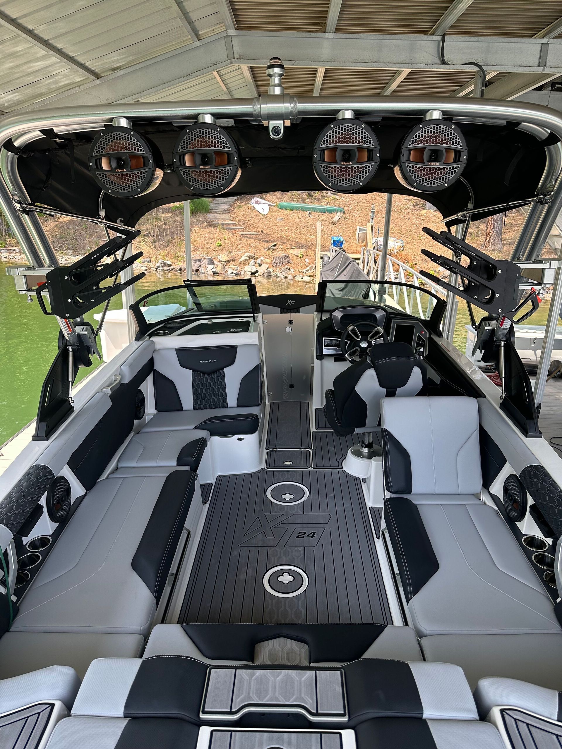 Boat interior with speakers, seating, and controls. White, gray, and black colors. Under a dock with a person visible.